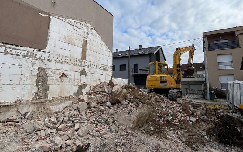 Bager uklanja ruševine srušenog objekta između zgrada